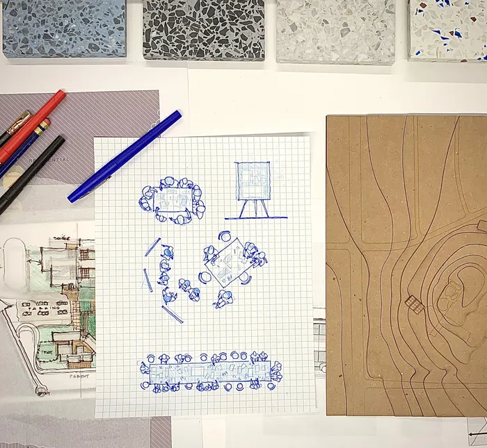 Overhead photograph of the studio desk: terrazzo samples, graph-paper sketches, and a topographic site model